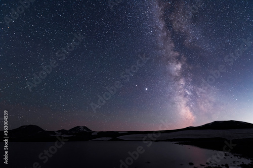 Beautiful night landscape. Alpine lake in the old volcanic mountains and beautiful bright milky way galaxy. Night photography.