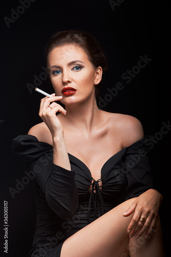 beautiful girl on a dark background in a dark dress looks into the frame with a cigarette in her hands and a hairdresser male hands