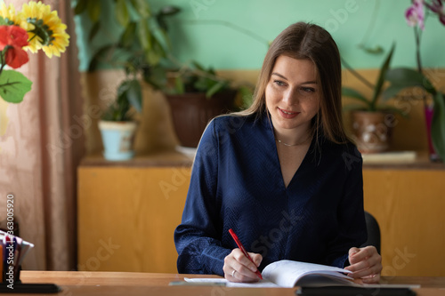 cheerful elegant young female teacher writing down in copybook w