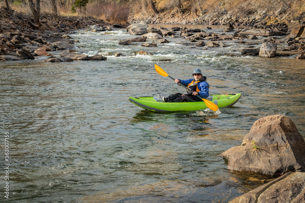 senior male kayaker  is paddling an inflatable whitewater kayak on a mountain river in early spring - Poudre River above Fort Collins, Colorado