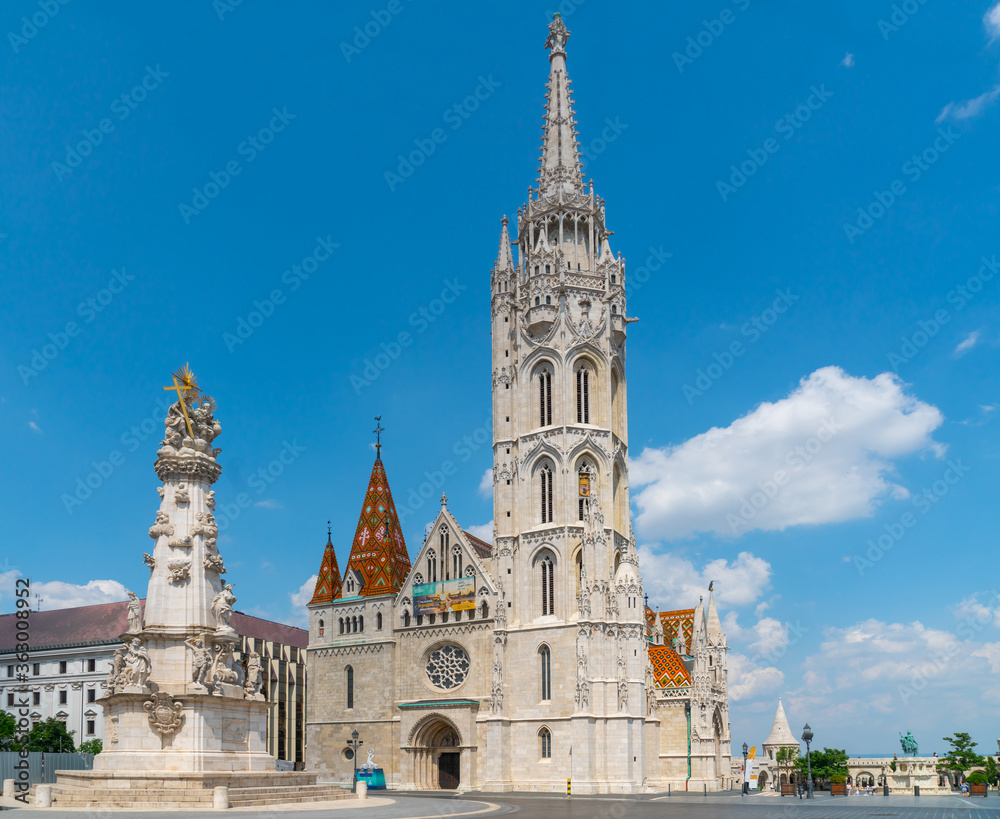 Budapest, Hungary - june 27th 2020 - Exterior of the  Matthias Church, with the Holy Trinity Statue in front during Corona time on a sunny day with some tourists visiting the church