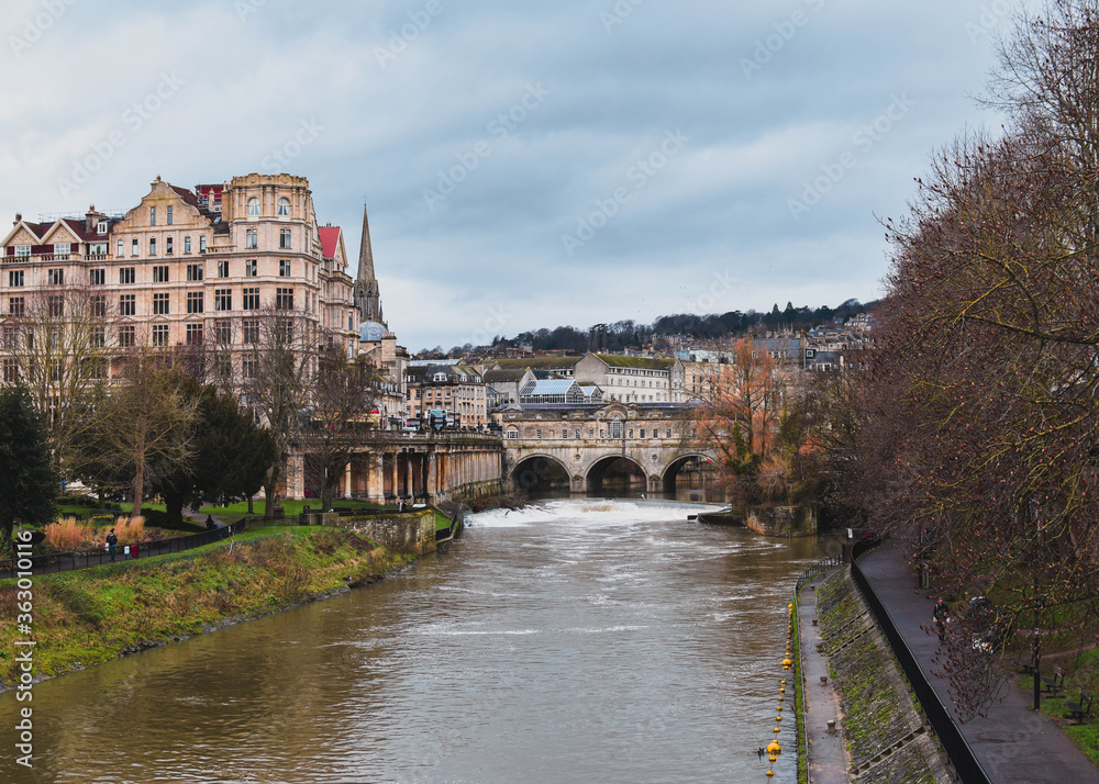 View of Bath City looking up the River Avon from the North Parade Bridge on an overcast day with a moody grey and blue sky in the background