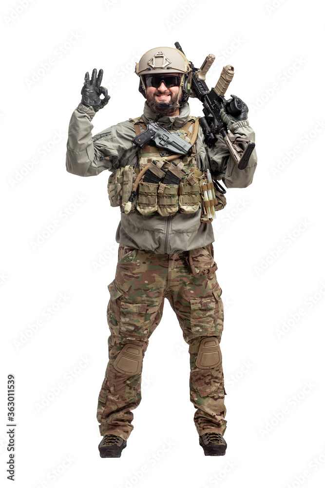 American soldier in military equipment with a rifle on a white background makes a good sign, commando with a weapon in uniform shows ok gesture American soldier in military equipment with a rifle on a white background makes a good sign, commando with a weapon in uniform shows ok gesture