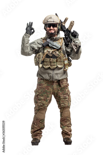 American soldier in military equipment with a rifle on a white background makes a good sign, commando with a weapon in uniform shows ok gesture