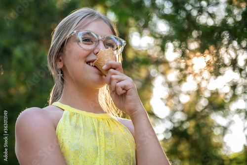 Cheerful teenager girl eating ice cream outdoor. Outdoor closeup portrait of girl eating ice cream in summer