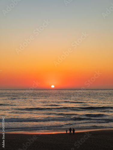 Vertical Image - Orange sunset lights up the sky and glows golden over the water and sandy beach © J Huser Photography