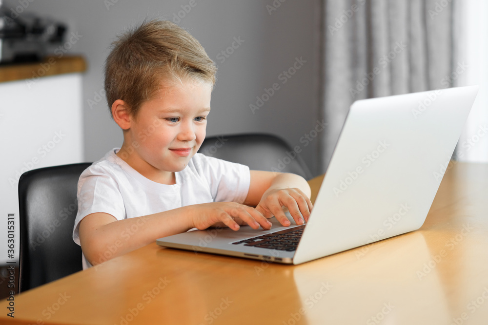 Funny young boy using a laptop computer sitting on top of a tableundefined at home Funny young boy using a laptop computer sitting on top of a tableundefined at home