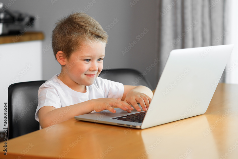 Funny young boy using a laptop computer sitting on top of a tableundefined at home Funny young boy using a laptop computer sitting on top of a tableundefined at home