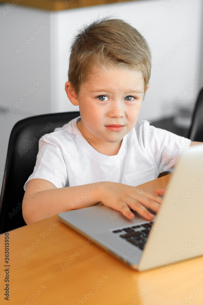 A young boy using a laptop computer sitting on top of a tableundefined at home A young boy using a laptop computer sitting on top of a tableundefined at home