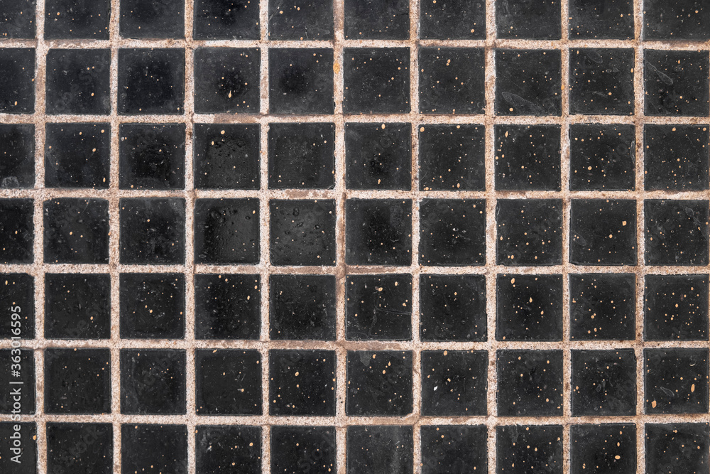 wall with gray stains of dirt, black square ceramic tiles with light cement. rough surface texture wall with gray stains of dirt, black square ceramic tiles with light cement. rough surface texture