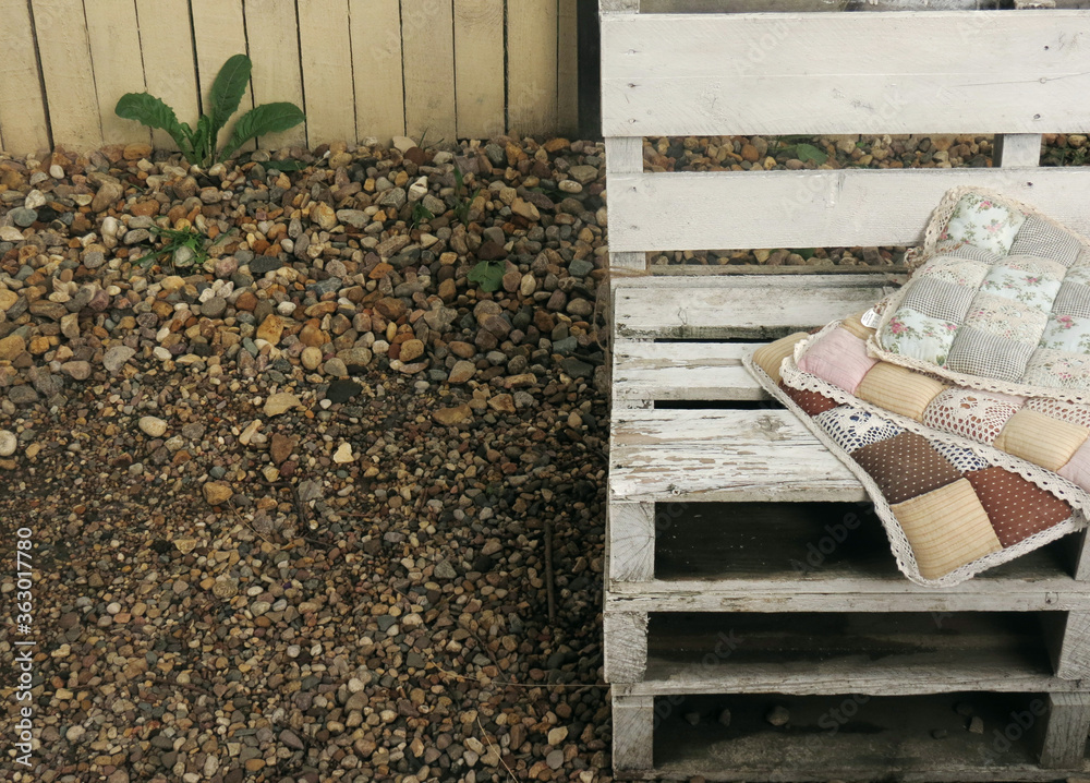 Soft pillows with floral print on a white wooden bench on the street, in the background a green dandelion and stones. Soft pillows with floral print on a white wooden bench on the street, in the background a green dandelion and stones.