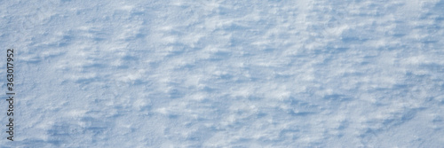 Natural snow texture. The surface of the snow crust. Snowy ground. Winter background with snow patterns. Closeup top view. Wide panoramic texture for background and design.