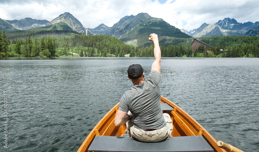 Wanderlust style travels. Milenials with bodybuilding silhouette sits in a boat. Freedom and joy while boating in a mountain lake.