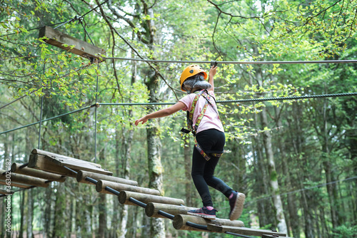 Tree climbing activity installations wooded area. A child walks on wooden bars. 