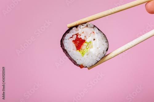 Tasty sushi roll maki with wooden chopsticks on pink background close up. Place for caption and text