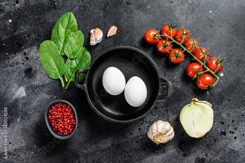 Ingredients for cooking Shakshuka. Eggs, onions, garlic, tomatoes, peppers, spinach. Black background. Top view