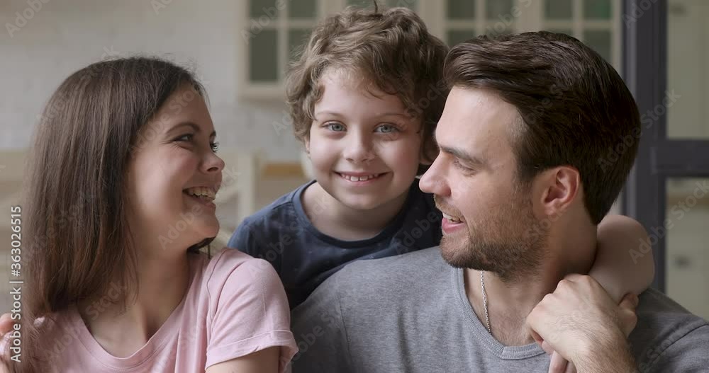 Happy family of three young parents with cute small adopted child son embracing having fun looking at camera bonding at home, loving mother father and little kid boy hugging, close up portrait Happy family of three young parents with cute small adopted child son embracing having fun looking at camera bonding at home, loving mother father and little kid boy hugging, close up portrait