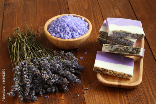 Sea salt with lavender in a bamboo bowl  soap made from lavender  olive oil and cocoa butter on a bamboo plate and dried lavender flowers are located on a brown wooden table. Closeup.