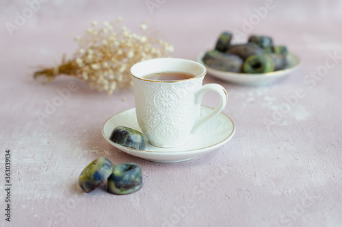 Raw vegan candy with raspberry and pistachio filling in chocolate coating. Served with a cup of tea on a light background,healthy sweets. Vintage. Copy space 