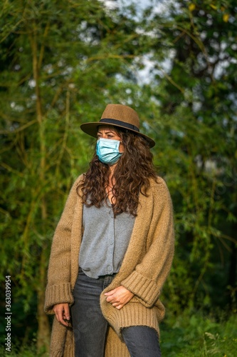Vertical shot of a young caucasian female with a medical mask on posing on a background of trees