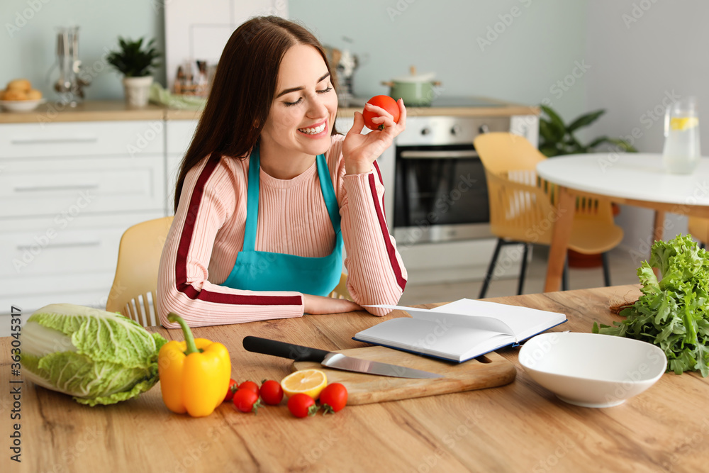 Young woman with recipe book and products in kitchen