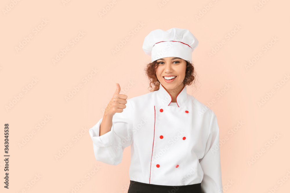 Female African-American chef showing thumb-up on color background