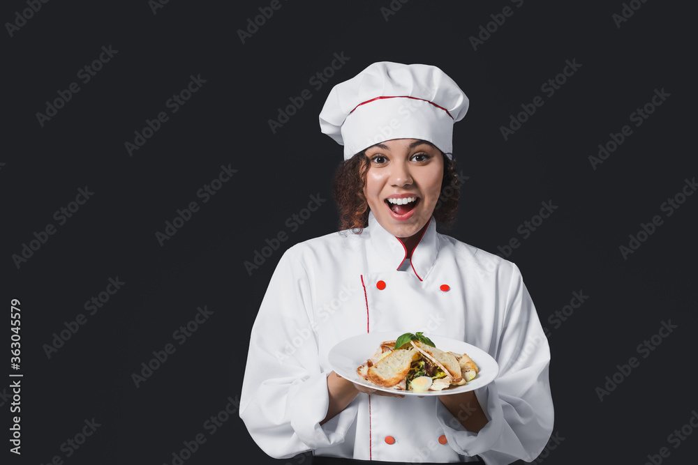 Female African-American chef with tasty dish on dark background Female African-American chef with tasty dish on dark background