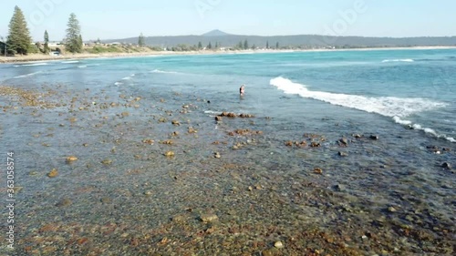 Aerial Drone Over Shallow Clear Ocean Water With Fisherman Standing On Rocks On Australian Beach photo