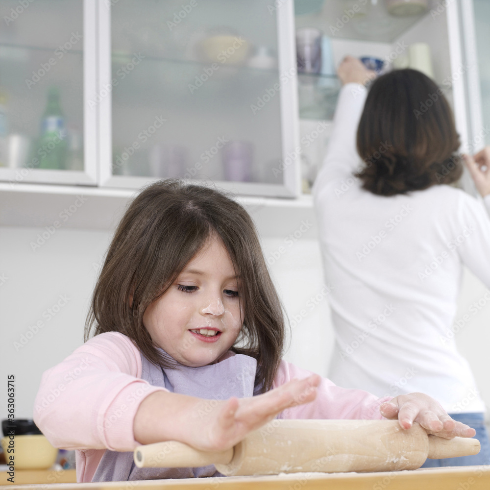 Girl using rolling pin with her mother in the background