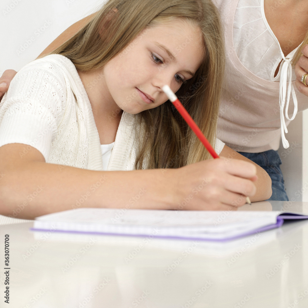 Girl writing, woman standing beside her Girl writing, woman standing beside her