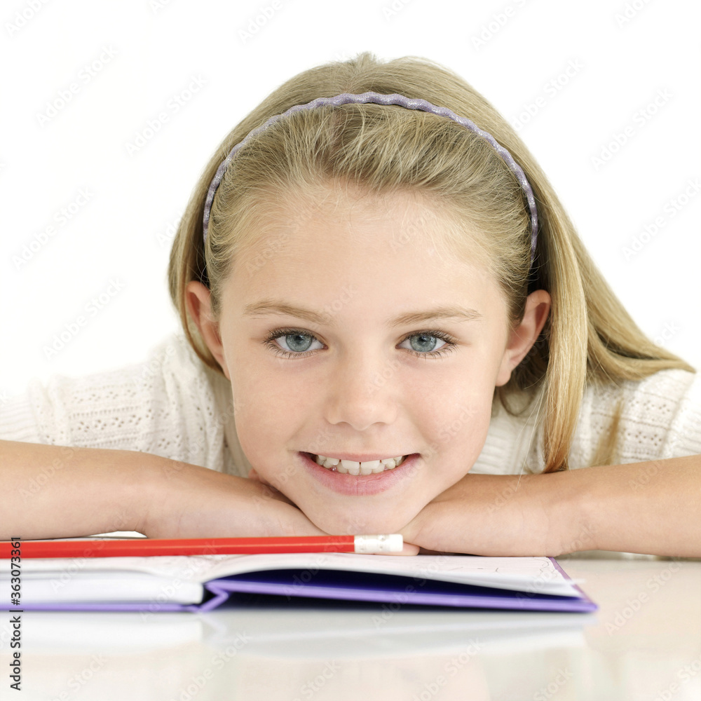 Girl smiling at the camera while resting her chin on book Girl smiling at the camera while resting her chin on book