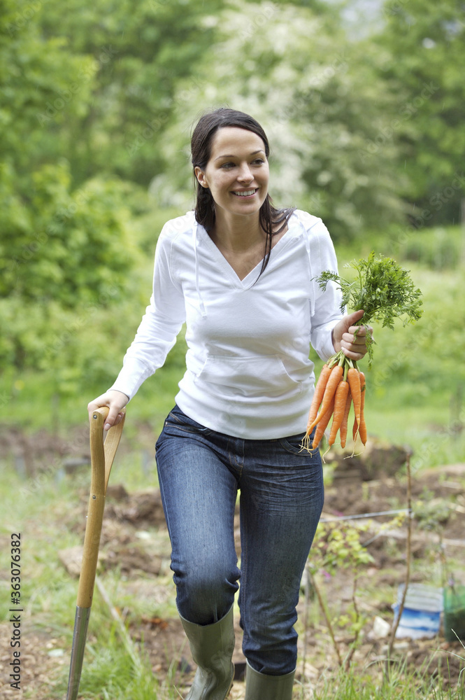 Obraz na plátně Woman holding carrots and spading fork