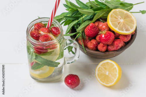 A bowl of berries and lemon and a mug of cold refreshing drink on a white table.