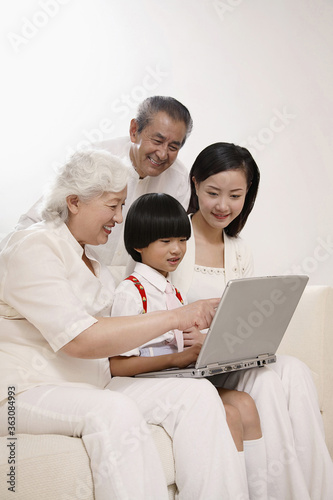 Senior woman teaching boy how to use laptop, woman and senior man watching