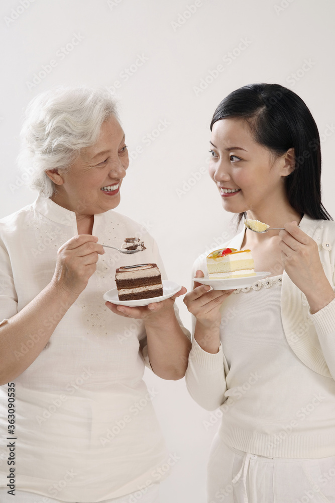 Senior woman and woman smiling at each other while enjoying their cakes Senior woman and woman smiling at each other while enjoying their cakes