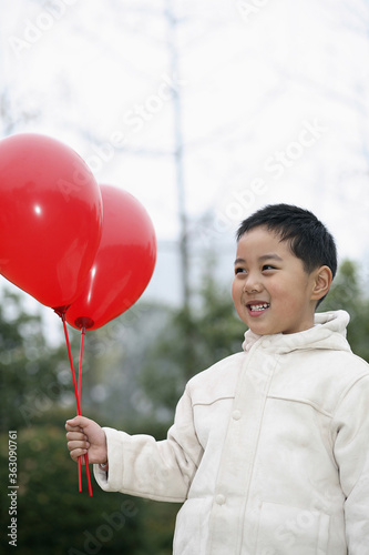 Boy smiling while looking at two red balloons
