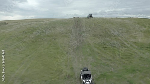 Exhilarating fast low flight of off-road buggy airborne on green dirt hillside road in flat countryside, Swift Current, Saskatchewan, Canada, rising aerial