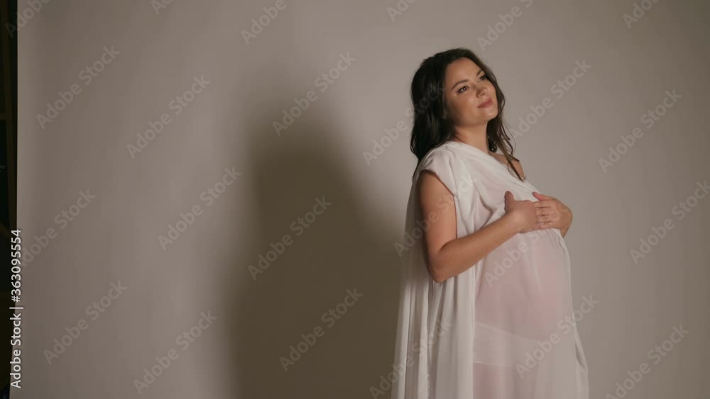 Beautiful pregnant Nude woman in white fluttering fabric on a white background. Slow motion. Portrait of a pregnant woman wrapped in a white cloth. Beautiful pregnant Nude woman in white fluttering fabric on a white background. Slow motion. Portrait of a pregnant woman wrapped in a white cloth.