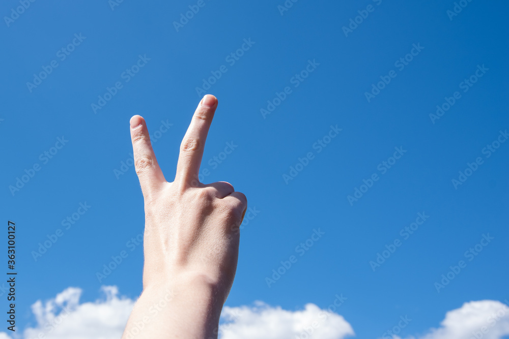 Hand with two fingers up in the symbol of peace or victory. Isolated on blue sky background with clouds, copy space. Hand with two fingers up in the symbol of peace or victory. Isolated on blue sky background with clouds, copy space.