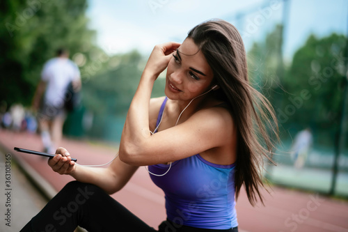 Beautiful woman resting from working out. Young athlete woman sitting on the bench and listening to the music. © JustLife