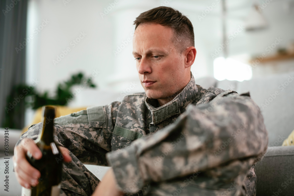 Depressed soldier with bottle sitting in livig room., Alcohol addiction.	