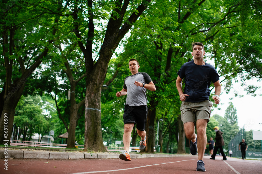 Young men training on a race track. Two young friends running on the athletics track	