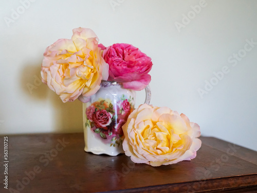 Foto Pink and yellow heritage roses in an old-fashioned jug with matching rose motif