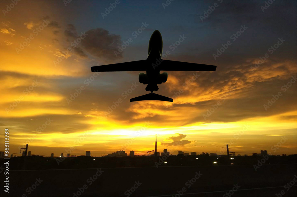 Silhouette airplane flying above big city in sun set time.  Airline business.