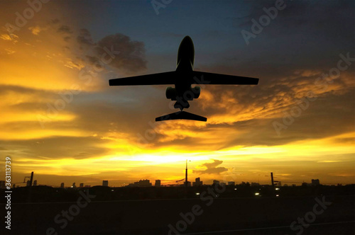 Silhouette airplane flying above big city in sun set time. Airline business.