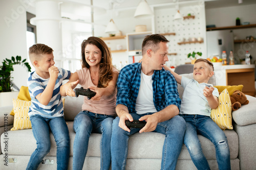 Husband and wife playing video games with joysticks in living room. Loving couple are playing video games with kids at home.  © JustLife