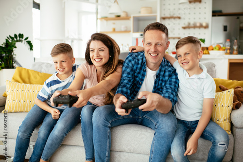 Husband and wife playing video games with joysticks in living room. Loving couple are playing video games with kids at home. 