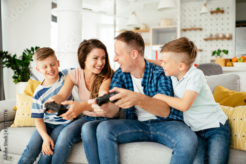 Husband and wife playing video games with joysticks in the living room. Loving couple are playing video games with kids at home. 