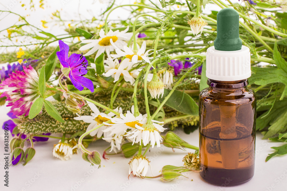 Dropper glass bottle with natural essential oil and a bouquet of wild flowers. Alternative medicine. Aromatherapy.