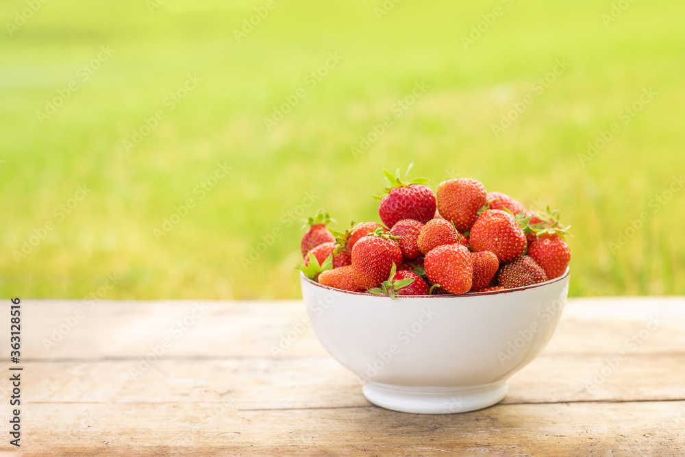 white plate with ripe strawberries on a wooden table on a background of greens white plate with ripe strawberries on a wooden table on a background of greens